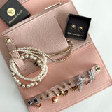 Travel jewelry roll by Chrysmela with pebbled vegan leather in delicate pink color with gold metal accents. plenty of storage for 6 pairs of earrings, necklace and ring bars, zippered wallet, and a wide pocket. light weight. A perfect travel companion to carry all the jewelry you need on the road.